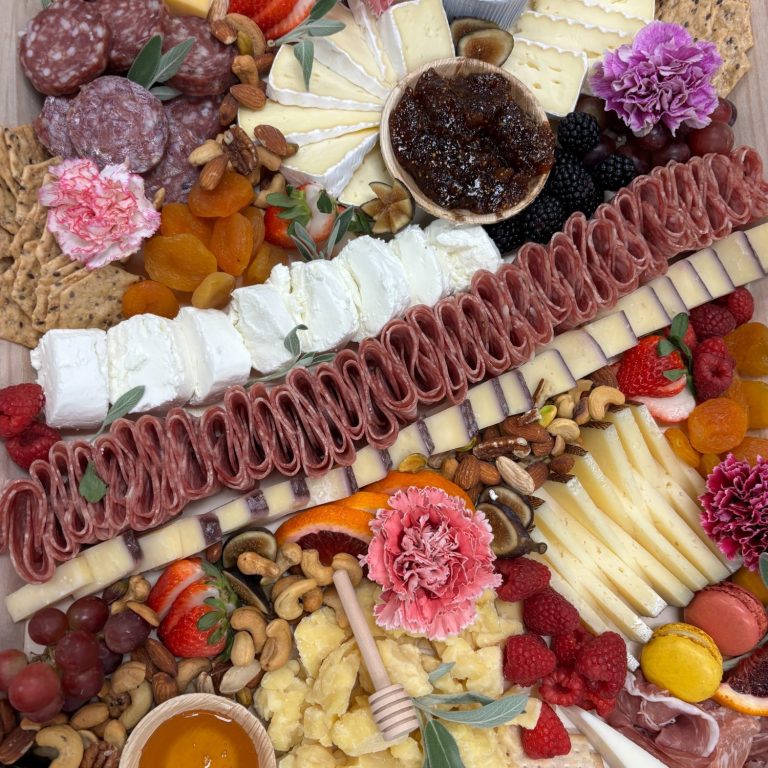 A colorful assortment of meats, cheeses, fruits, nuts, and honey.
